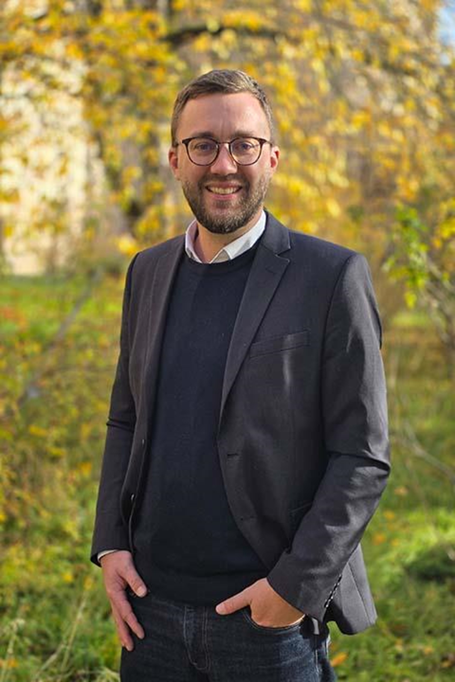 Es ist ein Mann zu sehen, der vor grünem Hintergrund in die Kamera lächelt. 