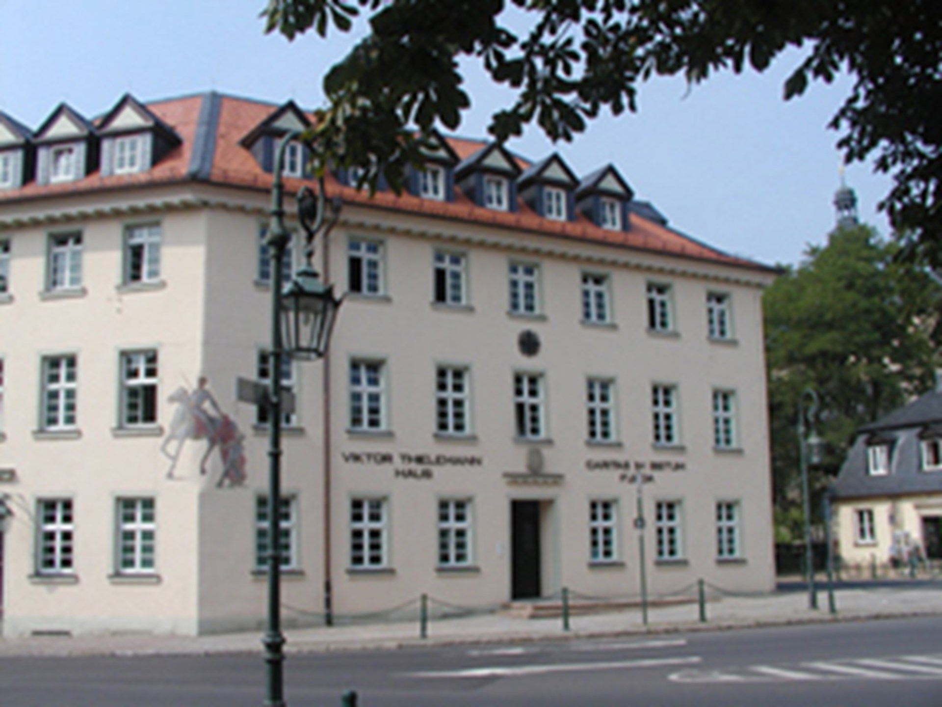 Ein helles dreistöckiges Gebäude mit einem roten Dach in dem viele Erker eingebaut sind, wird als Geschäftsstelle genutzt. 